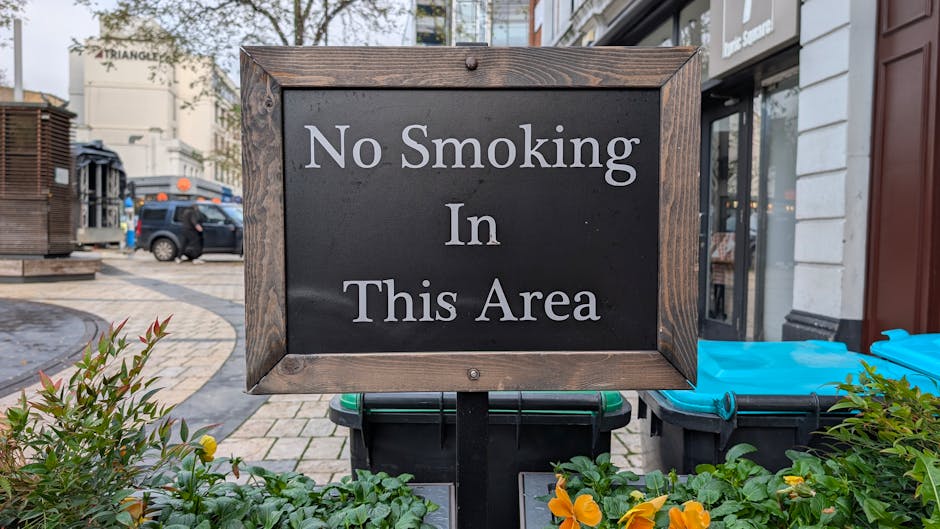A rectangular white sign with black uppercase lettering reading 'NO PARKING DAY OR NIGHT' is mounted on a light grey wooden door or wall. The sign is affixed with four metal screws, one in each corner